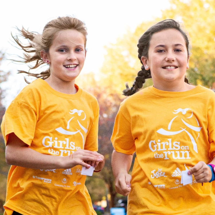 Two Girls on the Run participants in yellow shirts run while smiling at the camera